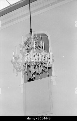 Chandelier, mairie, divers, 24-07-1970 Whizgle News, Dutch Desk, pays-Bas, 1950-2000 un lustre orné est élégamment suspendu au plafond, orné de motifs complexes et de bougies supportant plusieurs bras, tandis qu'un tissu drapé obscurcit une partie d'une fenêtre cintrée derrière lui. Banque D'Images