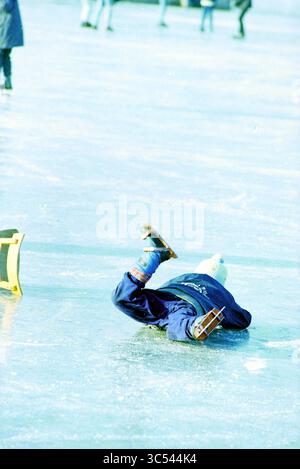 Divertissement sur glace dans la région, Haarlem, pays-Bas, 19-02-1994 Whizgle News, Dutch Desk, pays-Bas, 1950-2000 Un enfant en tenue d'hiver a subi un culbutement pendant qu'il patinait sur la glace, s'étendant de manière ludique sur la glace avec ses patins en l'air. À proximité, d'autres patineurs profitent de la patinoire, ajoutant à l'ambiance animée. Banque D'Images