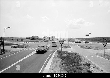 Crossing de Zilk, routes, construction de routes, plantation de routes, 29-06-1972 Whizgle News, Dutch Desk, pays-Bas, 1950-2000 Une scène vintage capture un rond-point avec des véhicules naviguant à l'intersection circulaire, entouré d'un paysage clairsemé et de quelques bâtiments au loin. Les panneaux routiers indiquent la direction et les points d'écoulement, tandis que les nuages dérivent au-dessus dans un ciel dégagé. Banque D'Images