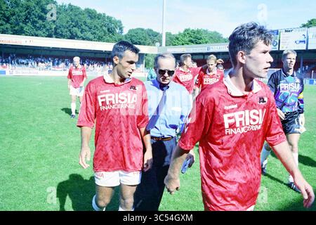 AZ - Telstar, 19-08-1995 Whizgle News, Dutch Desk, pays-Bas, 1950-2000 Un groupe de joueurs de football en maillots rouges avec « FRISIA FINANCIERING » sur la marche avant du terrain, paraissant concentré et déterminé. Ils sont accompagnés par un homme en chemise bleue, probablement un entraîneur ou un officiel de l'équipe, alors qu'ils se dirigent vers les lignes de touche après un match. Le stade est rempli de spectateurs en arrière-plan. Banque D'Images