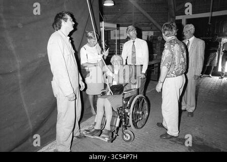 Une femme en fauteuil roulant monte une balle de farine dans un moulin à farine, 00-08-1991 Whizgle News, Dutch Desk, pays-Bas, 1950-2000 Un groupe de six personnes engage une conversation, avec une personne assise dans un fauteuil roulant. Le cadre semble être un espace intérieur avec des poutres en bois. Certaines personnes sont habillées en tenue formelle, tandis que d'autres portent des vêtements plus décontractés, créant une atmosphère diversifiée d'interaction et de soutien. Banque D'Images