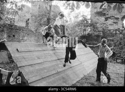 Waspetheater, Theater, 17-07-1981 Whizgle News, Dutch Desk, pays-Bas, 1950-2000 Un groupe de quatre personnes se livre à une activité de plein air ludique, une personne sautant d'une pente en bois tandis que les autres assistent ou observent. Le cadre présente un environnement envahi par la végétation, suggérant un sentiment d'aventure et de camaraderie. Banque D'Images