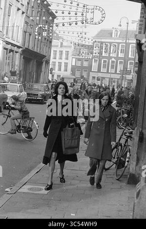 Shopping gens dans le centre-ville, gens et choses, Haarlem, Gierstraat, pays-Bas, 04-11-1973 Whizgle News, Dutch Desk, pays-Bas, 1950-2000 deux femmes se promènent dans une rue animée, vêtues de manteaux élégants, tandis que les gens naviguent à vélo et à moto à proximité. L'atmosphère est animée, avec des décorations festives au-dessus de la tête et de nombreux piétons engagés dans diverses activités, capturant une scène urbaine dynamique. Banque D'Images