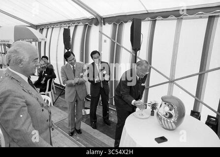 First pile Canon, Schiphol Z.O., Haarlemmermeer, 02-07-1990 Whizgle News, Dutch Desk, pays-Bas, 1950-2000 dans un cadre festif, un groupe d’hommes élégamment habillés se réunit autour d’une table avec une poupée décorative. Un homme est prêt à verser un verre sur la poupée tandis que les autres regardent avec des sourires et des applaudissements, créant une atmosphère de fête et de camaraderie. Banque D'Images