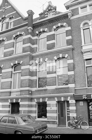 Bâtiments et fissures, Schotersingel 117, Huizen Haarlem, Haarlem, Schotersingel, pays-Bas, 27-01-1977 Whizgle News, Dutch Desk, pays-Bas, 1950-2000 la façade d'un bâtiment en briques vintage présente une alternance de bandes de briques claires et sombres, présentant de grandes fenêtres cintrées avec des détails décoratifs. Une voiture classique est garée à proximité, et un vélo s'appuie contre le mur, ajoutant à l'atmosphère pittoresque de la rue. L'entrée a un signe subtil visible, suggérant une activité à l'intérieur. Banque D'Images