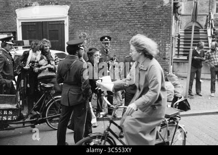 Campagne de verre de la mairie, vitraux, soufflage de verre, verre en général, Hôtel de ville de Haarlem, 01-10-1980 Whizgle News, Dutch Desk, pays-Bas, 1950-2000 Un groupe d'officiers en uniforme interagit avec une foule, tandis qu'une femme à vélo passe, portant un manteau et tenant un morceau de papier. En arrière-plan, diverses personnes s'engagent dans la conversation près d'un véhicule vintage contre un mur de briques texturé. Banque D'Images