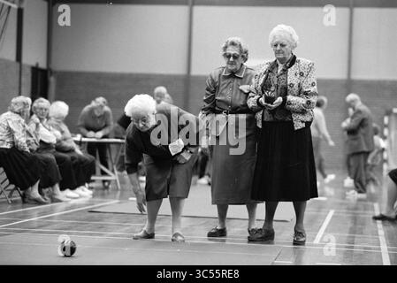 Koersbal, Zeewijk, IJm., IJmuiden, pays-Bas, 03-03-1992 Whizgle News, Dutch Desk, pays-Bas, 1950-2000 deux femmes âgées observent tandis qu'une troisième se plie pour faire rouler une boule de bowling sur un terrain, montrant la détermination et la concentration lors d'une compétition amicale. En arrière-plan, d'autres apprécient le jeu, créant une atmosphère animée. Banque D'Images