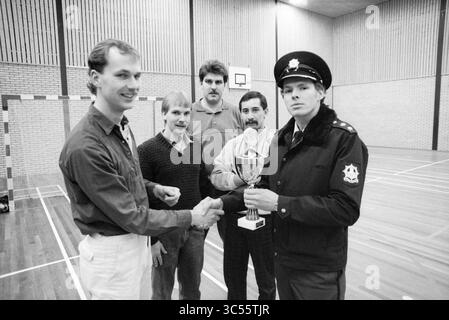 1er prix tournoi de football en salle Beverwijk, football en salle, Beverwijk, pays-Bas, 02-01-1987 Whizgle News, Dutch Desk, pays-Bas, 1950-2000 Un groupe de cinq hommes se tient debout dans une salle de sport, un homme en uniforme de police tenant un trophée tout en serrant la main d'un autre homme. L'atmosphère suggère une célébration d'une réussite sportive, avec les trois autres hommes regardant. Banque D'Images