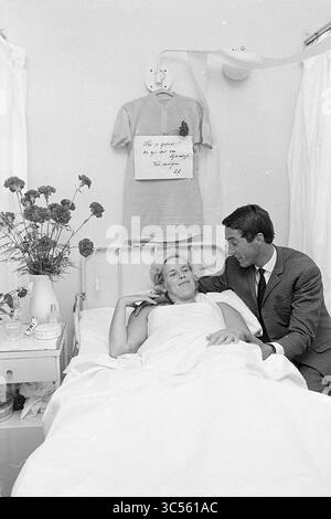 AB Geldermans with Wife., cyclisme, 22-07-1968 Whizgle News, Dutch Desk, pays-Bas, 1950-2000 Un homme est assis à côté d'une femme allongée dans un lit d'hôpital, échangeant des sourires chaleureux. Le lit est orné d'un bouquet de fleurs, et une chemise est accrochée au mur avec un message encourageant. L'atmosphère transmet un sentiment de soin et de compagnie. Banque D'Images