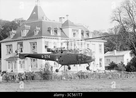 Princesse Margriet à Haarlem, réception à l'hôtel de ville, événements royaux, 16-10-1965 Whizgle News, Dutch Desk, pays-Bas, 1950-2000 Un hélicoptère militaire plane près d'un grand manoir élégant, avec une foule rassemblée au premier plan, regardant la scène se dérouler. Le bâtiment présente des détails architecturaux ornés, et des arbres entourent la zone, créant un contraste frappant entre l'avion moderne et la structure classique. Banque D'Images