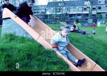 Ouverture du terrain de jeu Orionweg IJmuiden, IJmuiden, Nederland, 23-03-2002 Whizgle News, Dutch Desk, aux pays-Bas, 1950-2000 enfants jouent joyeusement sur un toboggan dans une aire de jeux en plein air dynamique, avec un enfant glissant vers le bas tandis que d'autres regardent et s'engagent dans diverses activités à proximité. La scène est remplie de rires et de l'énergie de la jeunesse ludique. Banque D'Images