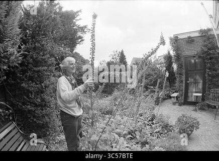 Femme posant dans (propre ?) Garden, 00-00-1993 Whizgle News, Dutch Desk, pays-Bas, 1950-2000 Une personne admire les plantes imposantes dans un jardin luxuriant, entouré de verdure et d'un charmant espace extérieur. L’atmosphère est sereine, capturant un moment de connexion avec la nature. Banque D'Images