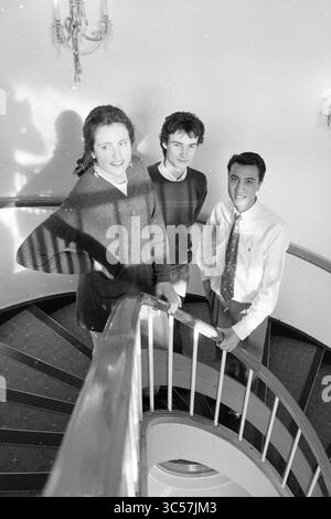 Leo van der Kar Fund, lauréats, 18-02-1991 Whizgle News, Dutch Desk, pays-Bas, 1950-2000 trois jeunes individus posent sur un escalier en colimaçon, avec un soupçon de jeu d'ombres dramatiques provenant de l'éclairage aérien. La femme se tient confiante à l'avant-garde, tandis que les deux hommes la flanquent de chaque côté, tous habillés dans une tenue décontractée mais élégante, donnant un sentiment de camaraderie et d'élégance détendue. Banque D'Images