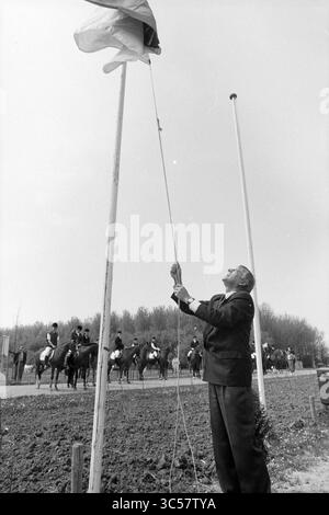 Ouverture du camp équestre et poney, Spaarnwoude, Spaarnwoude, 10-05-1991 Whizgle News, Dutch Desk, pays-Bas, 1950-2000 Un homme en tenue formelle lève un drapeau sur un poteau, tandis qu'un groupe de cavaliers montés peut être vu en arrière-plan, prêts et prêts. La scène capture un moment de cérémonie et de célébration dans un cadre naturel. Banque D'Images