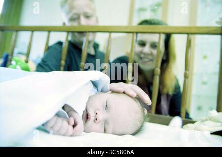 Family Van Bergen-Jacobs, Haarlem, pays-Bas, 14-11-2002 Whizgle News, Dutch Desk, pays-Bas, 1950-2000 Un bébé paisible dort dans un berceau, doucement emmailloté dans une couverture, tandis qu'un couple souriant regarde affectueusement, créant une atmosphère chaleureuse et aimante. Banque D'Images