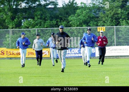 Première formation de l'équipe néerlandaise de baseball, Haarlem, pays-Bas, 26-05-1998 Whizgle News, Dutch Desk, pays-Bas, 1950-2000 Un groupe d'athlètes en uniforme de baseball fait du jogging délibérément sur un terrain pendant l'entraînement, mettant en valeur le travail d'équipe et le dévouement à leur entraînement. L'arrière-plan comprend une clôture à maillons de chaîne et une signalisation, soulignant une atmosphère d'installations sportives. Banque D'Images