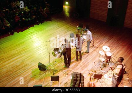 Grange de théâtre, rencontre des migrants, Haarlem, pays-Bas, 15-10-2003 Whizgle News, Dutch Desk, pays-Bas, 1950-2000 Une performance animée met en scène des musiciens jouant des casseroles en acier, avec un public assis captivé en arrière-plan. La scène capte l’énergie du moment, renforcée par un éclairage de scène illuminant les interprètes et leurs instruments. Banque D'Images