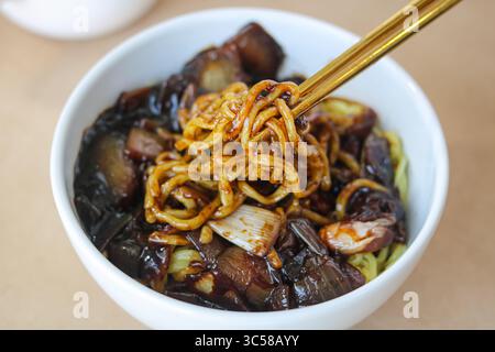 Manger un bol de Jajangmyeon avec des baguettes, un plat de nouilles coréen-chinois populaire. La sauce est faite de sauce aux haricots noirs avec de la viande et des légumes. Banque D'Images