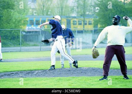 La première formation de l'équipe néerlandaise de baseball, 13-05-1997 Whizgle News, Dutch Desk, pays-Bas, 1950-2000 Un lanceur de baseball tire vers le haut pendant que deux coéquipiers observent depuis le terrain. Le décor est un diamant de baseball, avec un bus visible en arrière-plan. Banque D'Images