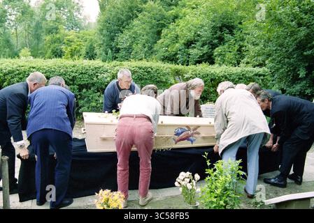 Funérailles Frans Verpoorten, Zwanenburg, Zwanenburg, 01-07-1997 Whizgle News, Dutch Desk, pays-Bas, 1950-2000 Un groupe de personnes se réunit autour d'un cercueil en bois, semblant le préparer à l'enterrement. Certains individus se penchent sur le cercueil, tandis que d'autres se tiennent à proximité, entourés de verdure et de fleurs. L'atmosphère semble réfléchie et sombre, suggérant un adieu ou un service commémoratif. Banque D'Images