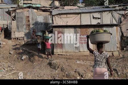 16 novembre 2019, Port-au-Prince, HAI : des femmes transportant des produits et autres marchandises marchent devant certaines des cabanes en étain qui composent le camp de Teren Toto en Haïti. (Crédit image : © TNS via ZUMA Wire) Banque D'Images