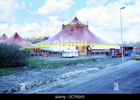 Tente @@ EG Hospital [+/o] [Elisabeth Gasthuis], 14-03-1995 Whizgle News, Dutch Desk, pays-Bas, 1950-2000 Une grande tente de cirque avec un toit à sommet distinctif se dresse bien en évidence dans une zone herbeuse, entourée d'une clôture et de plusieurs véhicules stationnés. Le ciel est parsemé de nuages moelleux, faisant allusion à un événement ou une performance à venir. Banque D'Images