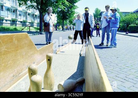 Journée nationale de jeux de rue, IJmuiden, 08-06-1999 Whizgle News, Dutch Desk, pays-Bas, 1950-2000 Un enfant vise en faisant rouler une balle vers un ensemble de quilles de bowling, tandis qu'un petit groupe de spectateurs regarde avec impatience dans un cadre extérieur animé. La scène capture l'esprit de compétition amicale et amusante. Banque D'Images