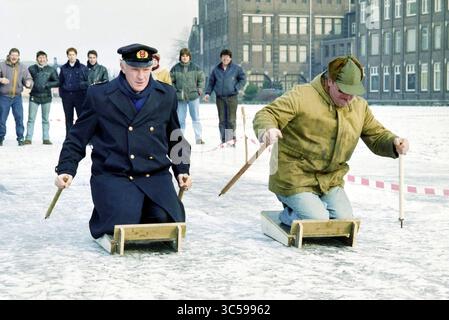 Personnel de traîneau à perche au bureau du port, 07-02-1996 Whizgle News, Dutch Desk, pays-Bas, 1950-2000 deux hommes sont engagés dans une compétition traditionnelle de patinage sur glace, assis sur des traîneaux en bois tout en se propulsant avec de longs perches. Derrière eux, un groupe de spectateurs regarde attentivement, ajoutant à l'atmosphère animée de cet événement hivernal. Banque D'Images
