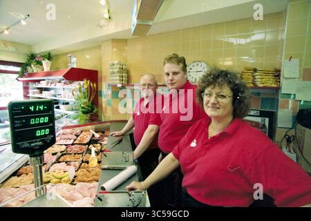 Chicken snack bar Bart, IJmuiden, IJmuiden, pays-Bas, 03-06-1999 Whizgle News, Dutch Desk, pays-Bas, 1950-2000 trois individus souriants se tiennent derrière une exposition de viandes et de produits alimentaires dans un magasin. Chacun porte une chemise rouge vif, et ils semblent prêts à aider les clients, avec une échelle et une horloge visibles en arrière-plan. L'atmosphère est animée et accueillante, mettant en valeur une entreprise locale dynamique. Banque D'Images
