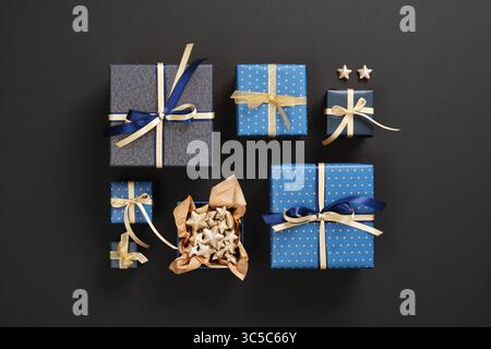 Une composition de cadeaux soigneusement arrangés de différentes tailles en papier bleu et avec des rubans dorés sur fond noir. Banque D'Images