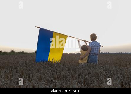 Une femme et un garçon tiennent un grand drapeau ukrainien debout dans un champ de blé au coucher du soleil. Symbole de la liberté et de l'indépendance de l'Ukraine. Les Ukrainiens veulent la paix. Banque D'Images