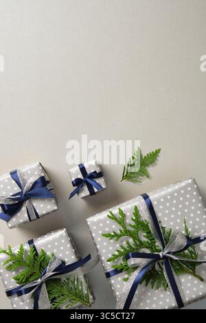 Coffrets cadeaux argentés soigneusement disposés avec des rubans bleus et des brins de thuya. Fond gris, espace pour votre texte. Banque D'Images