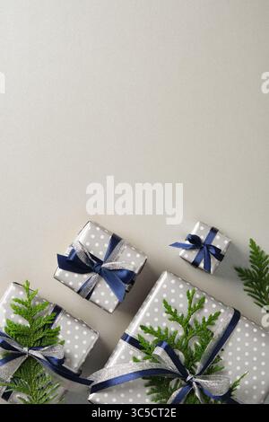 Coffrets cadeaux argentés soigneusement disposés avec des rubans bleus et des brins de thuya. Fond gris, espace pour votre texte. Banque D'Images