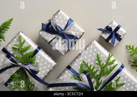 Coffrets cadeaux argentés soigneusement disposés avec des rubans bleus et des brins de thuya. Fond gris Banque D'Images