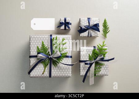 Coffrets cadeaux argentés soigneusement disposés avec des rubans bleus et des brins de thuya. Fond gris Banque D'Images