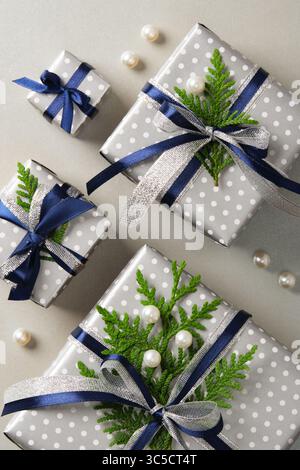Coffrets cadeaux argentés soigneusement disposés avec des rubans bleus et des brins de thuya. Fond gris Banque D'Images