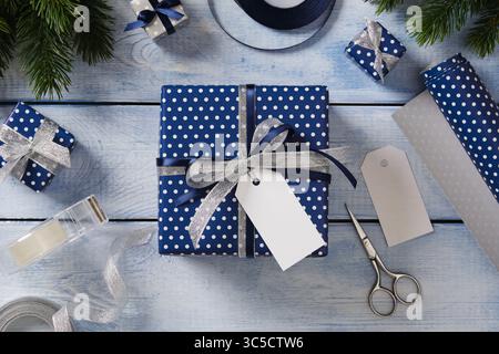 Articles d'emballage pour cadeaux. Rouleaux de papier d'emballage, ciseaux, ruban, cadeaux prêts à l'emploi. Fond en bois bleu, espace pour votre texte. Banque D'Images