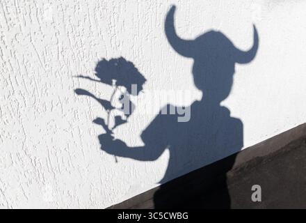 Ombre drôle sur le mur d'un enfant dans des cornes vikings tenant une fleur. Jeu d'ombre et de lumière du soleil. Jeux d'enfance et d'imagination. Idées créatives f Banque D'Images
