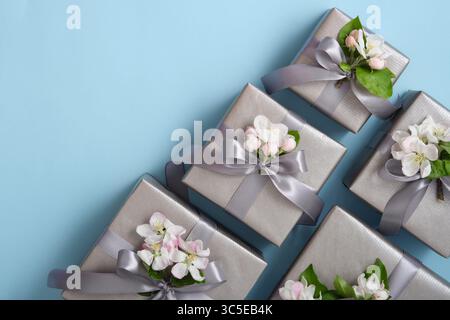 Boîtes cadeaux grises avec des fleurs de pomme et des rubans argentés sur fond bleu clair. Horizontal, espace pour votre texte. Banque D'Images