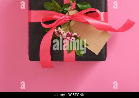 Boîte cadeau noire d'artisanat avec étiquette vierge, fleurs d'aubépine sur fond rose. Place pour votre texte Banque D'Images