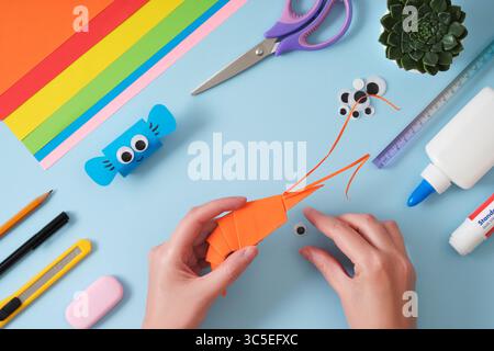 Faire une crevette origami avec du papier orange. Mains de femmes tenant l'engin. Hobby Idea, un jouet pour les enfants. Banque D'Images
