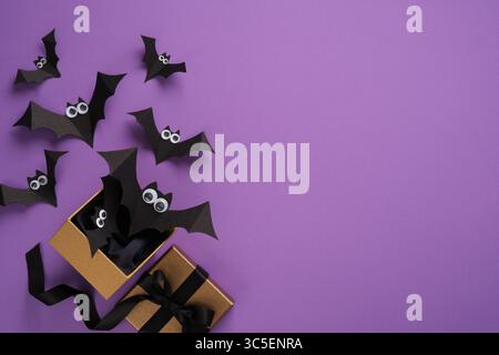 Les chauves-souris en papier volent hors d'une boîte cadeau sur un fond violet. Fond pour les cartes d'halloween, les bannières, les invitations. Place pour votre texte. Banque D'Images