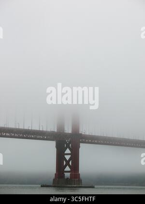 Vue rapprochée d'un pilier du Golden Gate Bridge s'élevant d'un épais brouillard matinal à San Francisco, sa structure rouge partiellement cachée par la douce brume. Banque D'Images