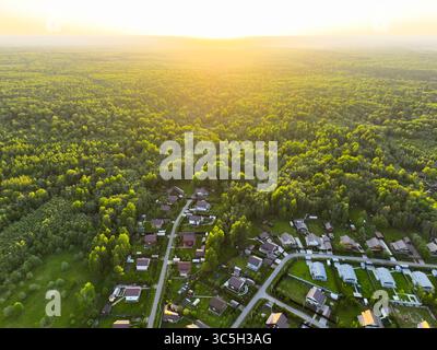 Une photo aérienne capture la lueur chaude du coucher de soleil sur une forêt verdoyante tentaculaire avec un village rural niché au premier plan Banque D'Images