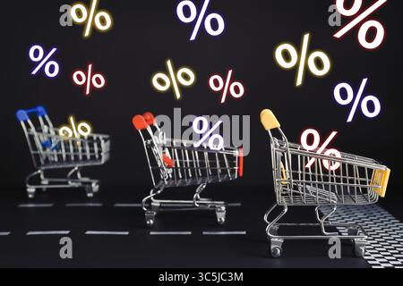 Les signes de pourcentage volent hors des chariots de course sur fond noir. Vente chaude, offre spéciale Banque D'Images