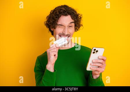 Jeune homme dans un pull vert tenant un smartphone et souriant sur un fond jaune vif présentant une carte Banque D'Images