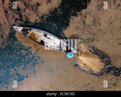 Vue aérienne d'un pêcheur solitaire jetant un filet d'un bateau en bois altéré au milieu des eaux troubles de Rajbari, division de Dhaka, Bangladesh. Banque D'Images