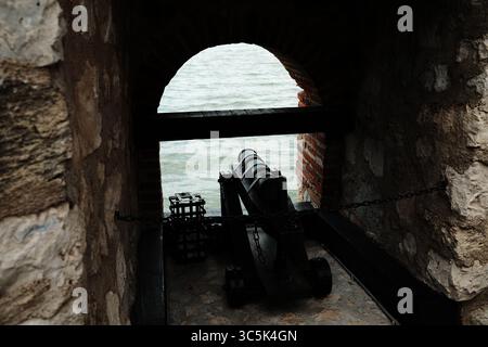 Canon historique à l'intérieur de la forteresse Golubac pointant vers le Danube, vu à travers une fenêtre voûtée en briques. Vue dégagée avec éclairage spectaculaire Banque D'Images