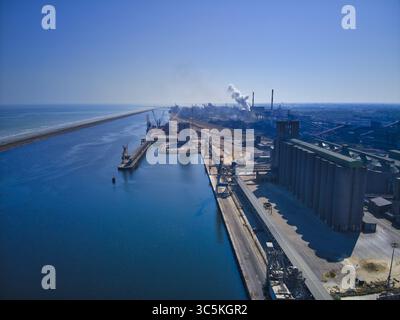 Vue aérienne du port industriel contrastant la mer bleue profonde avec les structures en béton gris, Dunkerque, Nord, France. Banque D'Images