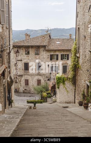 Vue sur les anciens bâtiments en pierre bordent une rue en pente, baignée de lumière douce, un tableau pittoresque de l'architecture italienne et du charme, Gubbio, Ombrie, Italie. Banque D'Images